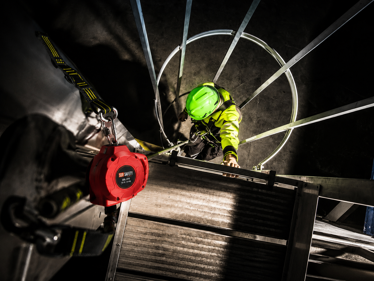 Técnico ascendiendo por escalera con jaula en una operación vertical industrial
